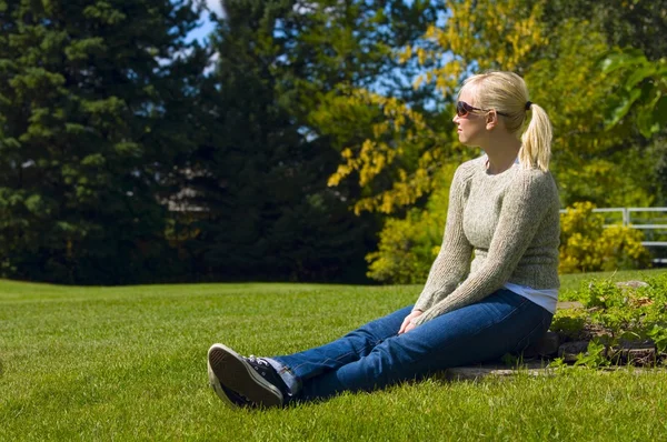 Jonge vrouw zitten in het gras — Stockfoto