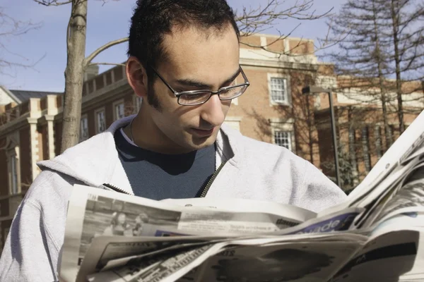 Молодой человек читает газету снаружи — стоковое фото