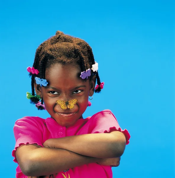 Africana niña con brazos cruzados y una mariposa en su nariz —  Fotos de Stock
