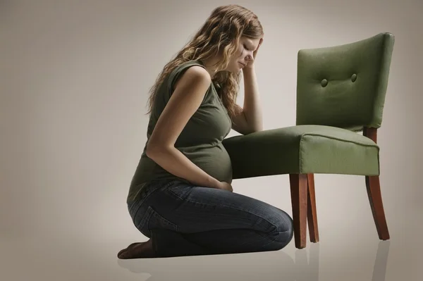 Una donna incinta triste seduta vicino alla sedia — Foto Stock