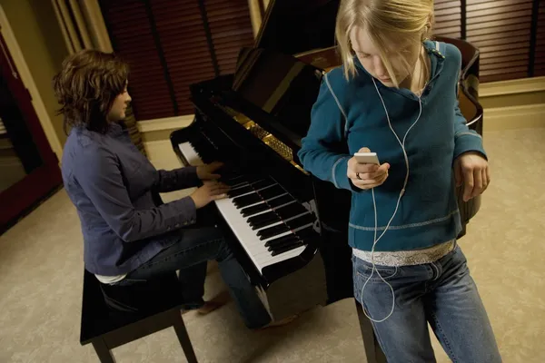 Chica escuchando música otro toca el piano —  Fotos de Stock