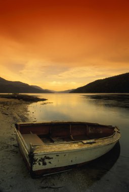 Old Rowboat At Water's Edge With Sunset Background clipart