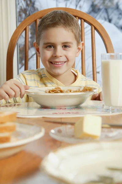 Mladý chlapec jíst obilí u stolu se snídaní — Stock fotografie