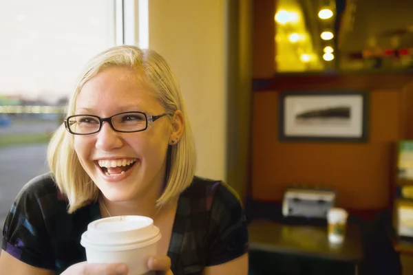 Ung kvinna leende med kaffe på ett kafé — Stockfoto