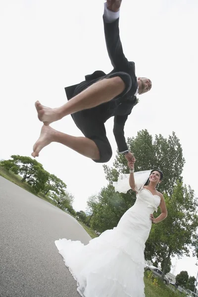 Жених прыгает в воздух, держа руку невесты — стоковое фото