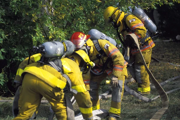 Feuerwehrmänner vor der Tür holen Feuerwehrschlauch — Stockfoto