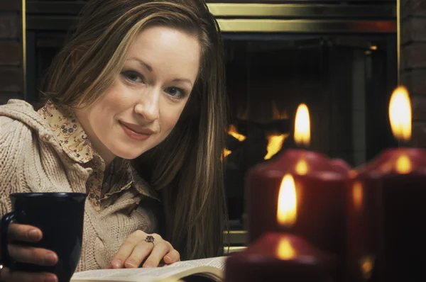 Joven mujer leyendo libro delante de la chimenea — Foto de Stock