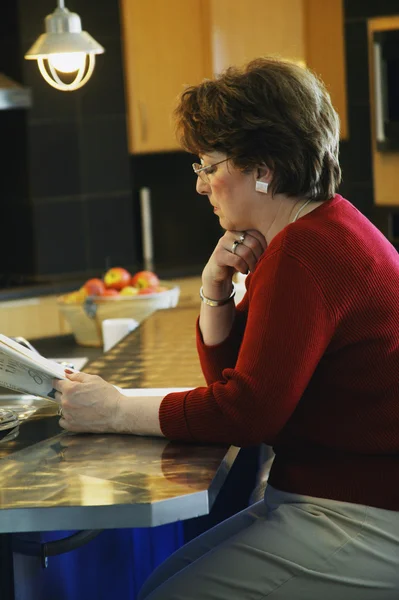 Woman reading a newspaper in the kitchen — Stock Photo, Image