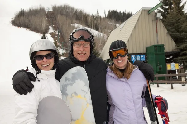 Tre adulti in una stazione sciistica, con snowboard e sci in mano — Foto Stock