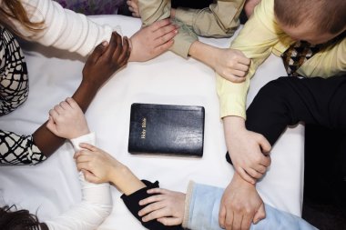 Group Of People Praying Around A Bible clipart