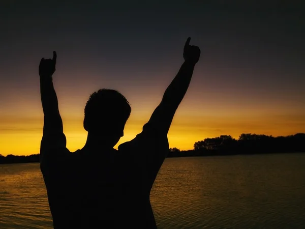 Людина з руками, підняв, як він дивиться на захід сонця над озеро — стокове фото