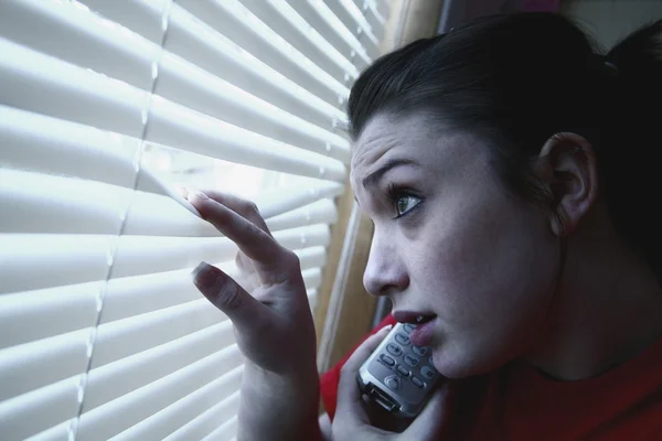 Adolescente no telefone, espreitando uma janela — Fotografia de Stock