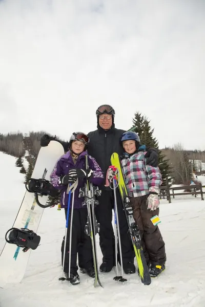 Father And Two Daughters At A Ski Resort Holding A Snowboard And Skiis — Stock Photo, Image