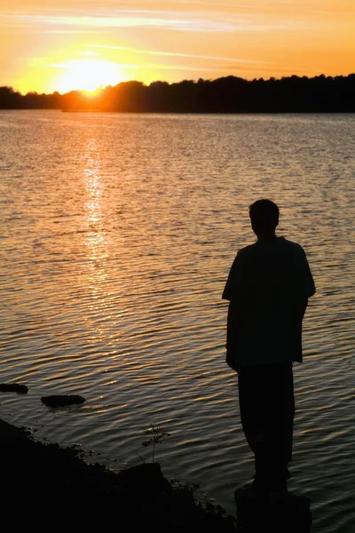 Silhouet van een man die op de oever kijken naar de zonsondergang — Stockfoto