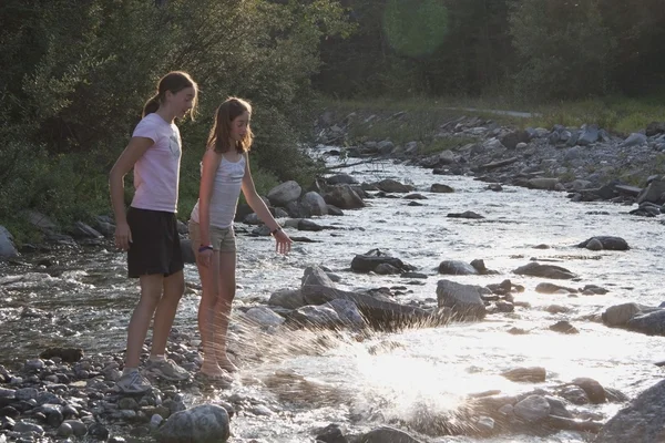 Две девушки бросают камни в реку — стоковое фото