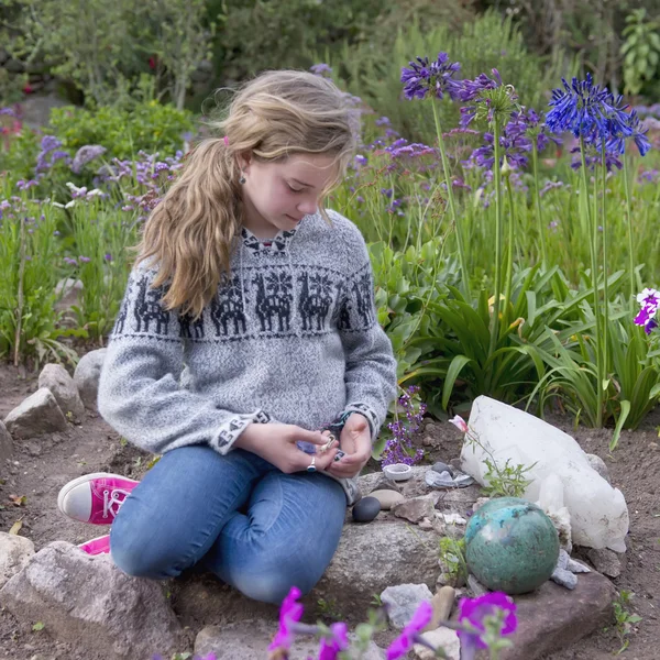 Mädchen sitzt auf Steinen neben einem Blumengarten — Stockfoto