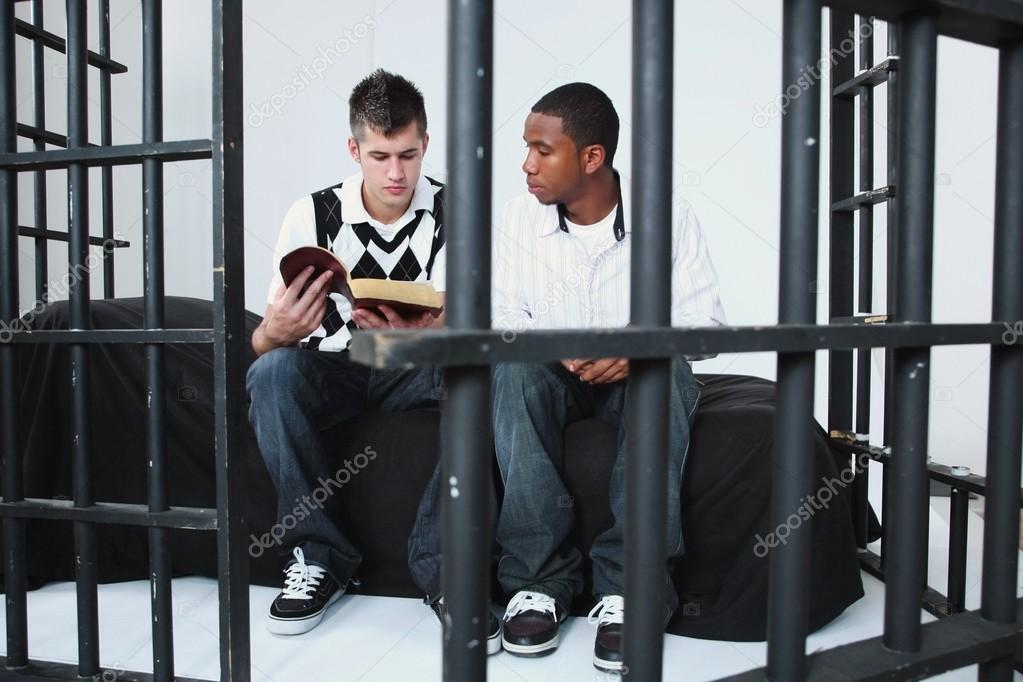 Young Man Reading The Bible To Another Young Man In Jail