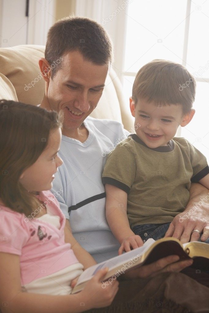 Father Reading The Bible To His Young Son And Daughter