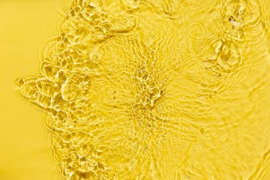 Waves on clear water surface, yellow abstract background.