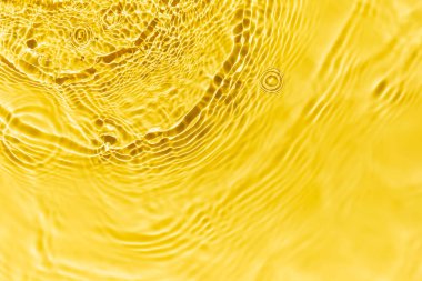 Waves on clear water surface, yellow abstract background.