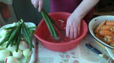 Yaşlı bir kadın yeşil soğan yıkıyor. 