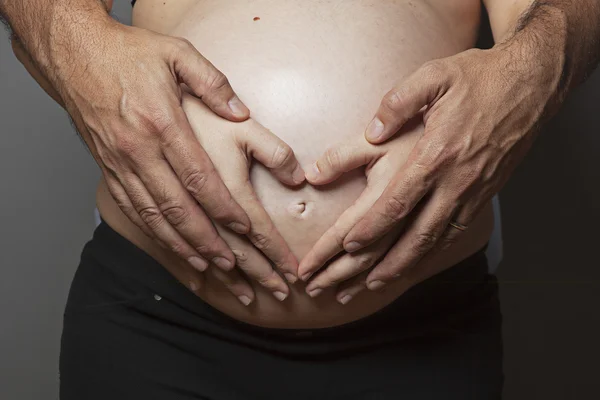 Hands forming a hearth on the pregnant belly — Stock Photo, Image