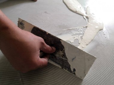 İnşaat işçileri kendi seviyelerini yükseltme metodunu kullanarak zemine lastik döşeme için bir malayla kendi seviyelendirme bileşimini yayıyorlar..