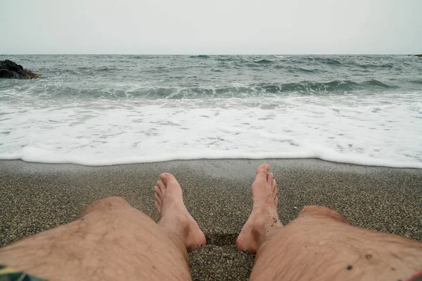 Close Man Legs Sitting Sand Receiving Waves Sea Subjective Shot — Foto de Stock