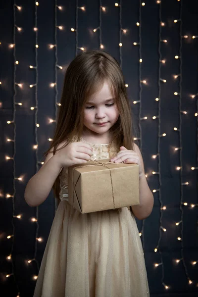 Gyönyörű, arany ruhás kislány boldog karácsonyt kíván. Képeslap az új évre. A gyermek mosolyog és csodáról álmodik. Bokeh a háttérben. — Stock Fotó