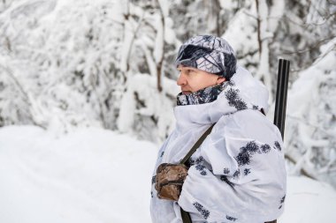 Omzunda bir silahla kış ormanında beyaz bir komando kıyafeti giymiş bir erkek avcı. Boşluğu kopyala.