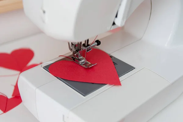 Máquina de costura e corações de papel. O processo de fazer uma grinalda. Conceito para costurar com amor, Dia dos Namorados. Fotografia De Stock