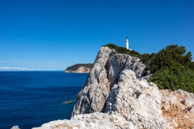 İyonya 'nın sarp kayalıkları, üzerinde yeşil deniz feneri olan kayalıklar. Yunanistan 'da açık mavi gökyüzü yaz günü. Manzaralı seyahat yeri. Lefkada Adası