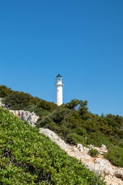Yunanistan 'da açık mavi bir günde, kayalıklarda yürüyüş yolu olan yeşil uçurumdaki Yunan beyaz deniz feneri. Manzaralı seyahat yeri. Lefkada adası. Dikey
