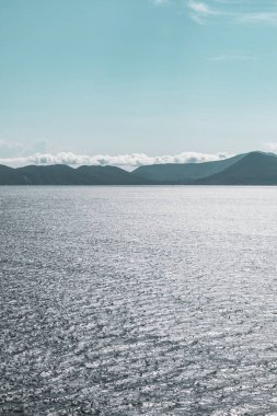 Lefkada Yunanistan adasındaki mavi İyon deniz manzarası. Uzak adaların üzerinde alçak bulutlarla aydınlık bir gün. Dikey derecelendirilmiş deniz arkaplanı