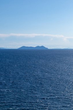 Lefkada Yunanistan adasındaki mavi İyon deniz manzarası. Uzak adaların üzerinde alçak bulutlarla aydınlık bir gün. Dikey deniz arka planı
