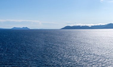 Mavi Akdeniz manzarası. Lefkada Yunanistan adasındaki İyon deniz manzarası. Uzak adaların üzerinde alçak bulutlar ve suyun üzerinde kontrastlı güneş ışığıyla aydınlık bir gün.