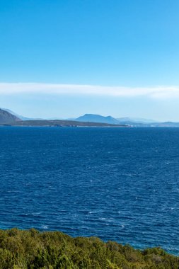 Açık mavi bir günde, Yunan adalarında deniz kıyısında yeşillik. Fırtınalı dalgalı su ve mavi gökyüzü. Lefkada adası, İyon deniz kıyısı, Yunanistan. Dikey