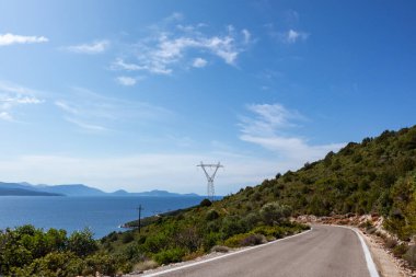 Yeşil canlı tepeleri ve berrak mavi manzarası olan dik kırsal bir yolda ilerliyoruz. Lefkada adasını gez, Yunanistan. Güneşli yaz manzaralı gündüz gezisi