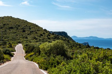 Yeşil canlı tepeleri ve berrak mavi gökyüzü olan sarp ve sarp bir yolda ilerliyoruz. Lefkada adasını gez, Yunanistan. Güneşli yaz manzaralı gündüz gezisi