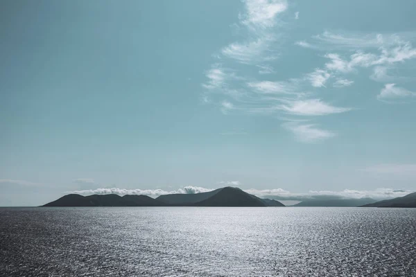 Lefkada Yunanistan adasındaki mavi İyon deniz manzarası. Uzak adaların üzerinde alçak bulutlar ve suyun üzerinde kontrastlı güneş ışığıyla aydınlık bir gün. Renk sınıflandırılmış