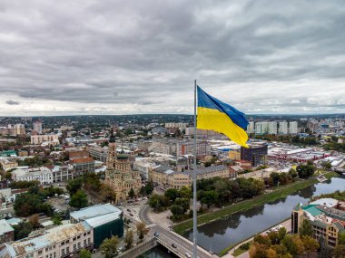 Ukrayna 'nın sarı ve mavi bayrağı bayrak direğinde dalgalanırken, destansı ağır bulut manzarası, sonbahar nehri Lopan seti üzerinde şehir havası, Ukrayna' nın Kharkiv kentindeki Kutsal Annunciation Katedrali