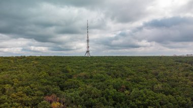 Telekomünikasyon kulesi antenli ve bulutlu gri destansı gökyüzü olan hava manzaralı karanlık orman. Kharkiv, Ukrayna