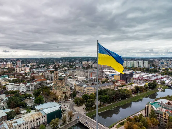 Ukrayna 'nın sarı ve mavi bayrağı bayrak direğinde dalgalanırken, destansı ağır bulut manzarası, sonbahar nehri Lopan seti üzerinde şehir havası, Ukrayna' nın Kharkiv kentindeki Kutsal Annunciation Katedrali