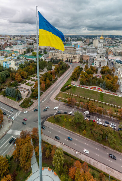 Флагшток с флагом Украины, осенняя красочная городская вертикальная панорама вблизи набережной реки Лопан, Сквер Стрилка, Успенский собор в Харькове, Украина