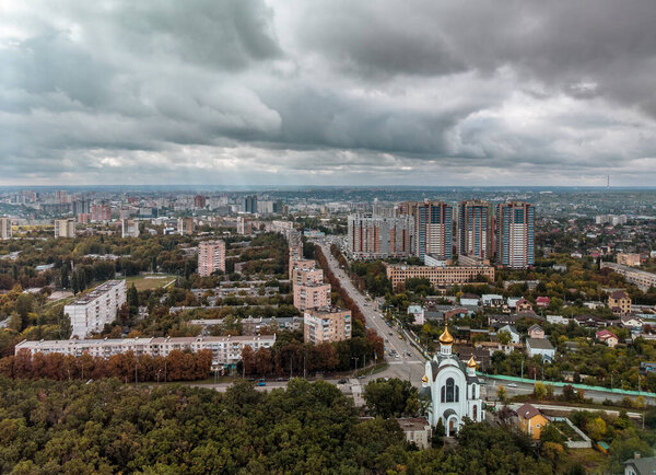 Cityscape aerial with dramatic clouds. Kharkiv city Pavlovo Pole district, view on Nauky ave, church and multistory high residential buildings from autumn forest