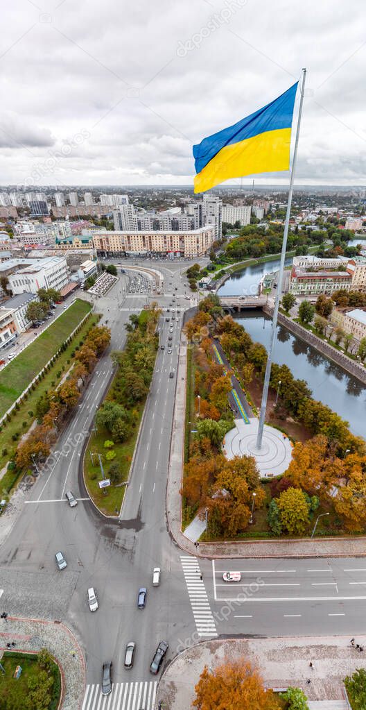 Tallest flagpole with flag of Ukraine in Europe, autumn colorful city aerial vertical view on Sobornyi Descent crossroad near river Lopan embankment, Skver Strilka in Kharkiv, Ukraine