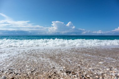 Yunanistan 'ın Lefkada adasının sahillerinde mavi fırtınalı dalgalar ve destansı bulutlu beyaz köpüklü manzaralı manzaralı çakıl taşı plajı. İyon Denizi 'ne yaz tatili