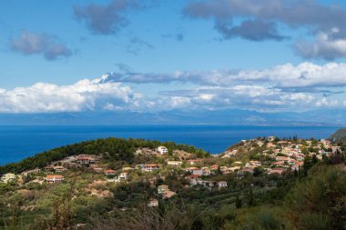 Yunanistan 'ın Lefkada adasında mavi deniz kıyısına yakın yeşil tepelerde turuncu kiremitli çatıları olan geleneksel Yunan köyü. Yazın Avrupa seyahati