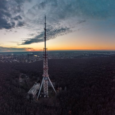 Telekomünikasyon kulesi anten silueti ile karanlık ormandaki hava günbatımı manzaralı bulutlu gökyüzü. Kharkiv, Ukrayna