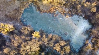 Sıcak gün batımında, ormanda, donmuş, küçük, vahşi göle yukarıdan bakan hava manzarası. Kışın, güneşli, buzlu göletin üzerindeki yüksek ağaç manzarası..